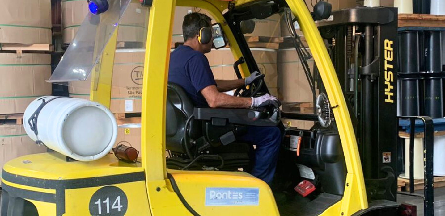 Operador dirigindo uma empilhadeira Hyster amarela em um armazém, equipado com sistema de monitoramento WEG