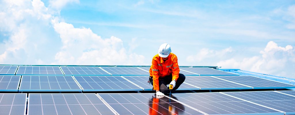 Trabalhador instalando painéis solares sob céu azul claro.