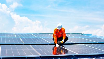 Trabalhador instalando painéis solares sob céu azul claro.