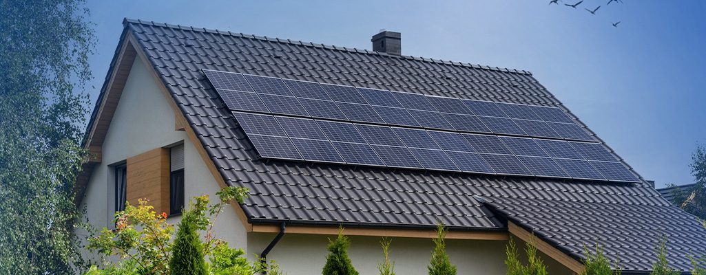 Casa residencial com painéis solares instalados no telhado, simbolizando energia limpa e sustentável, cercada por árvores e vegetação verde.