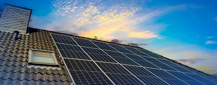 Imagem de um telhado com painéis solares instalados sob um céu ao entardecer, promovendo energia limpa e sustentável.
