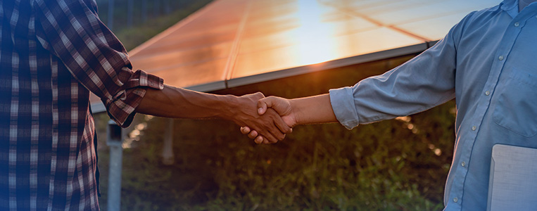 Duas pessoas se cumprimentando com um aperto de mão ao pôr do sol, simbolizando parceria e acordo.