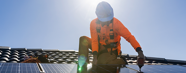 Técnico instala painéis solares em telhado ao sol, promovendo energia renovável e sustentabilidade no ambiente residencial.