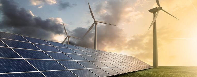 Painéis solares em primeiro plano com turbinas eólicas ao fundo, sob céu com nuvens e luz de pôr do sol, representando variações de geração de energia.