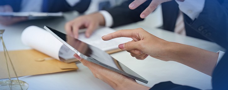 Mãos apontam para um tablet sobre uma mesa com documentos e pasta, sugerindo conferência de checklist e revisão de informações.