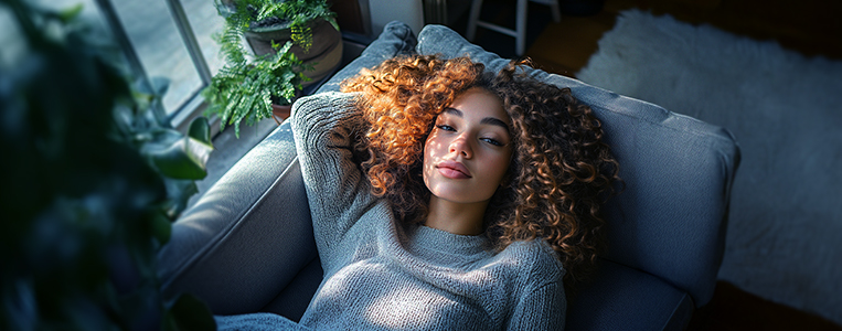 Mulher de cabelos cacheados deitada em sofá.