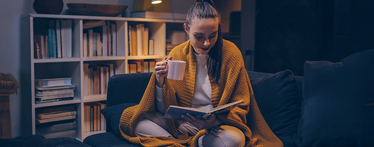 Mulher lendo um livro enquanto toma um café na companhia de um gato de estimação em um ambiente acolhedor e bem iluminado, ideal para momentos de relaxamento e leitura, evidenciando uma atmosfera tranquila e confortável.