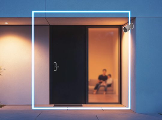Imagem de uma fachada moderna com iluminação neon azul em volta de uma porta de vidro, mostrando uma pessoa sentada dentro, na fachada de uma casa contemporânea.