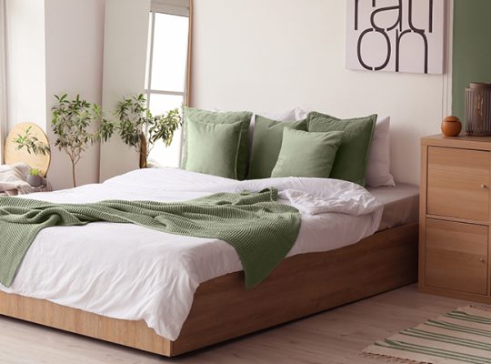 Quarto decorado com cama de madeira, almofadas verdes, roupa de cama branca e decoração moderna com plantas e obra de arte na parede.