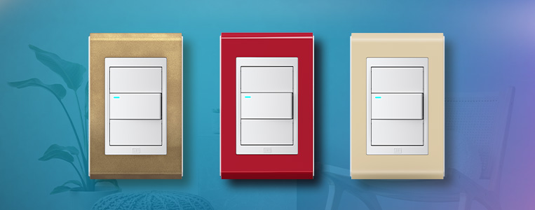Três interruptores de luz em cores variadas - bege, vermelho e branco, instalados em uma parede azul clara, destacando-se por sua simplicidade e funcionalidade.
