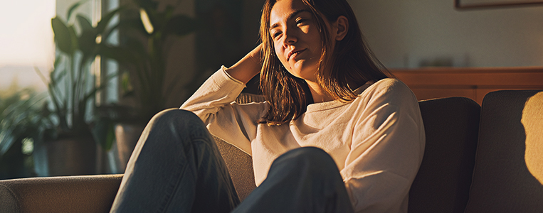 Pessoa sentada no sofá, em ambiente doméstico com luz natural, em pose contemplativa, representando hábitos e expectativas do consumidor em casa.