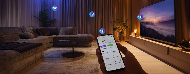 Mão segura um smartphone com app de automação aberto em uma sala com TV; ícones de Wi‑Fi indicam dispositivos conectados.