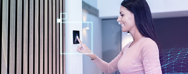 Pessoa sorrindo aciona um interruptor/painel inteligente na parede em um ambiente moderno, simbolizando uso simples da automação.